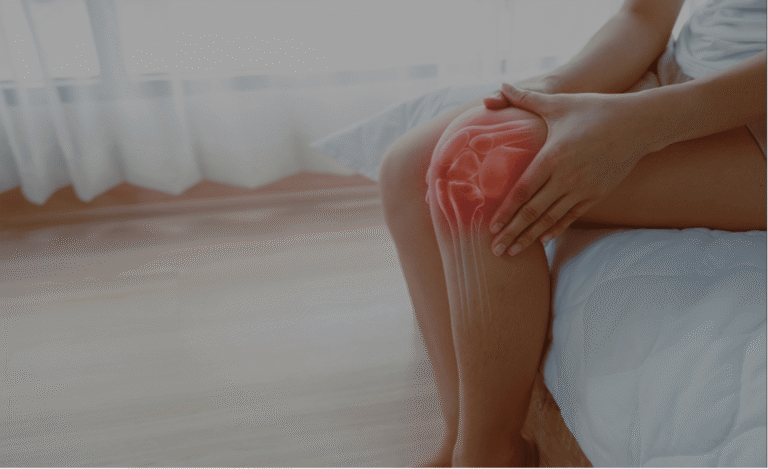 Frau sitz auf Bettkante, hält sich Knie, Haut auf Knie durchscheinend sodass das Gelenk sichtbar ist. Gelenk rundherum rot-orange eingefärbt