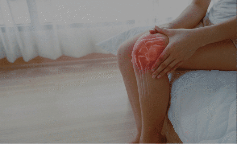 Frau sitz auf Bettkante, hält sich Knie, Haut auf Knie durchscheinend sodass das Gelenk sichtbar ist. Gelenk rundherum rot-orange eingefärbt